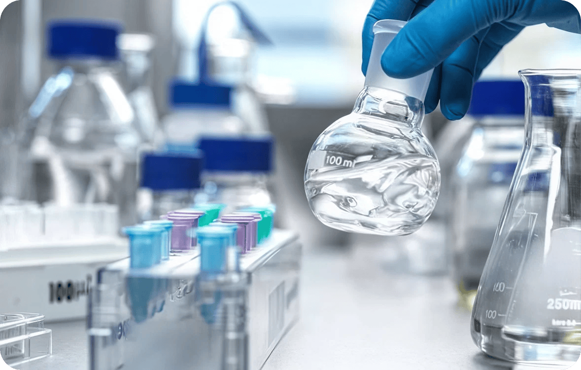 Gloved hand holding a flask of clear water among lab testing equipment