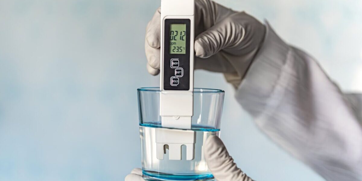 pH meter in hands with gloves, glass of water on a blue background. Measurement of the characteristics of drinking water. The hardness of the water. poor water quality. high values of salt impurities